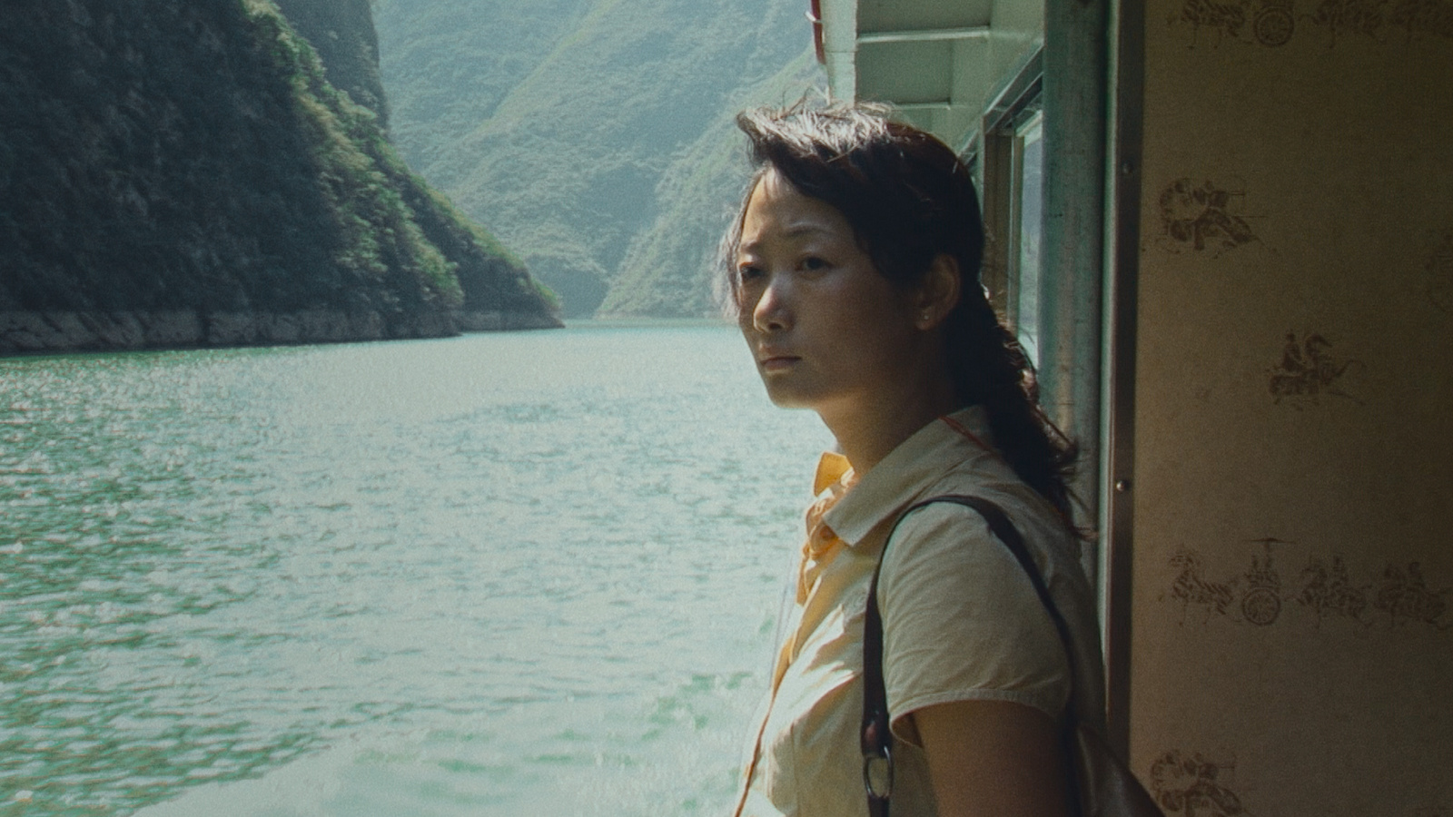 Official Caught by the Tides film still showing a woman beside a boat window overlooking a river gorge