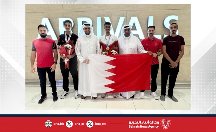 Bahrain cyclists at an airport welcome with medals and the Bahrain flag.